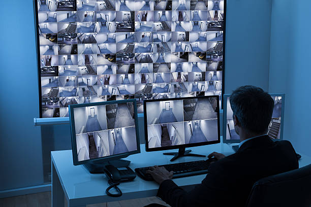 rear view of a man in control room monitoring multiple cctv footage rear view of a man in control room monitoring multiple cctv footage